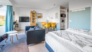 Una habitación de hotel moderna con cama, sofá, escritorio con sillas, televisor y estantería.