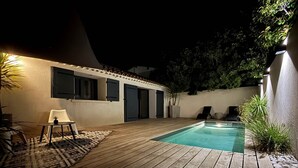 Una terrassa de fusta amb una piscina, una cadira blanca i una taula petita.