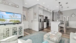 A modern living room with a flat-screen TV, a dining area with a wooden table, and a kitchen with white cabinets and stainless steel appliances. - 60 seconds to the Beach Harmony Shores Beach, Pool, Lagoon all just steps away (Gulf Shores)