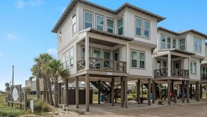 A two-story beachfront building with balconies, a sandy ground floor, and palm trees. - 60 seconds to the Beach Harmony Shores Beach, Pool, Lagoon all just steps away (Gulf Shores)