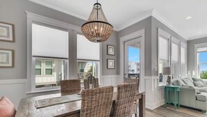A dining area with a wooden table and wicker chairs, a hanging light fixture, and large windows with a view of the outside. - 60 seconds to the Beach Harmony Shores Beach, Pool, Lagoon all just steps away (Gulf Shores)