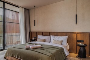 Une chambre à coucher moderne avec un grand lit, une tête de lit en bois et une vue dégagée grâce à de grandes fenêtres du sol au plafond.