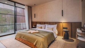 Een moderne slaapkamer met een groot bed, een nachtkastje, een stoel en uitzicht door een raam met dunne gordijnen.