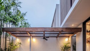 Een terras buiten met een houten pergola, een zithoek en een barbecue.
