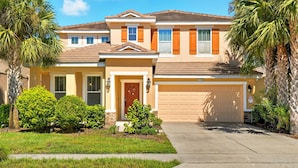 A two-story house with a front garage, a well-maintained lawn, and palm trees.