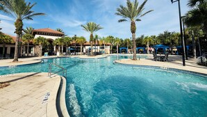 A swimming pool with a clear blue water, surrounded by palm trees and lounge chairs.
