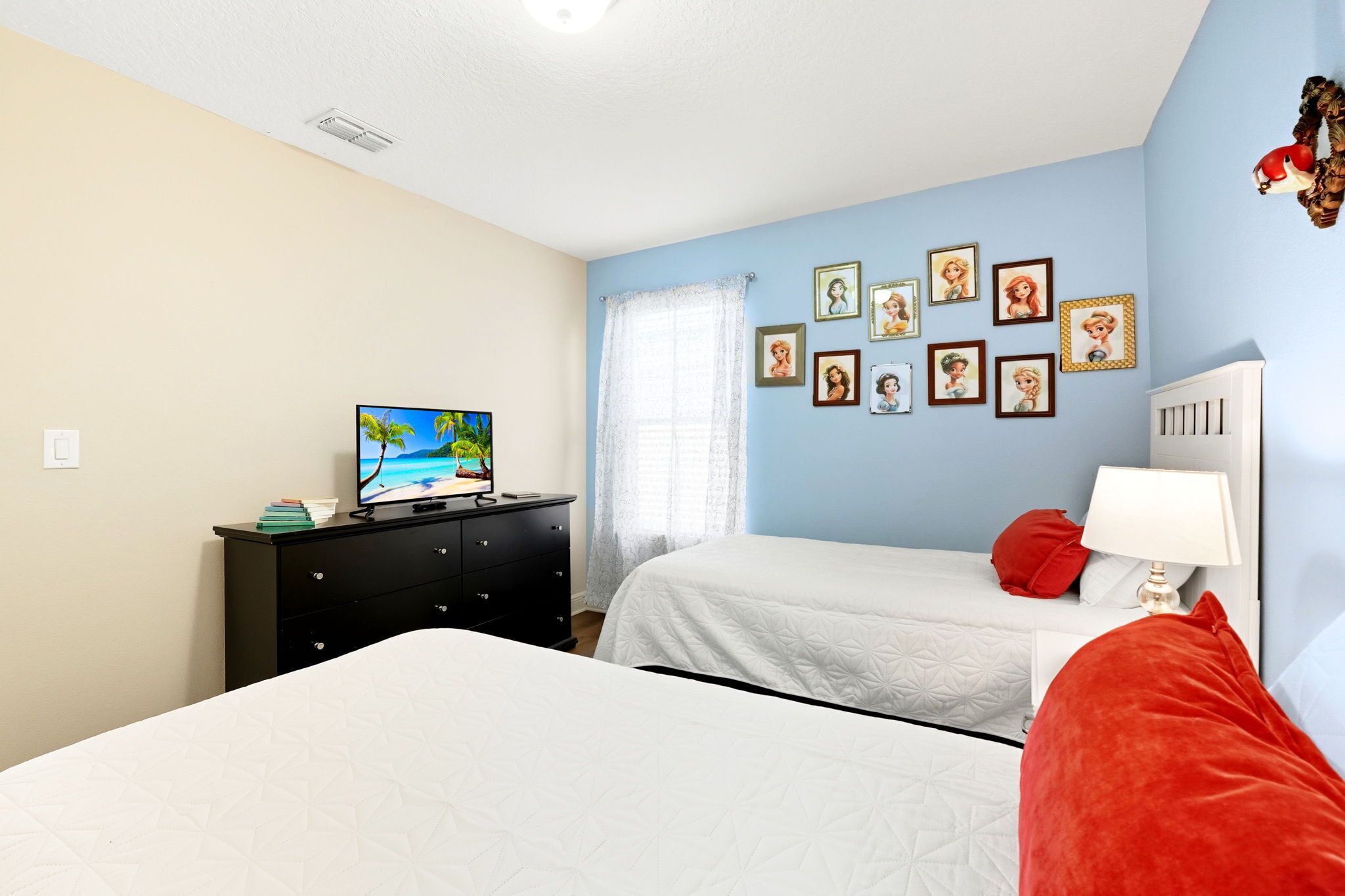 A bedroom with two beds, a TV on a dresser, and several framed pictures on the wall.
