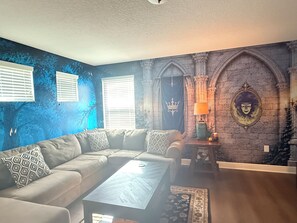 Een woonkamer met een hoekbank, een salontafel, een wanddecoratie, een open haard en een lamp.