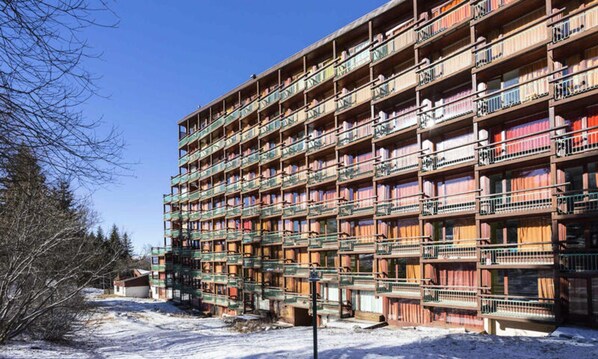 Ein mehrstöckiges Gebäude mit Balkonen, vermutlich ein Hotel oder eine Wohnanlage, bei blauem Himmel und Schnee auf dem Boden.