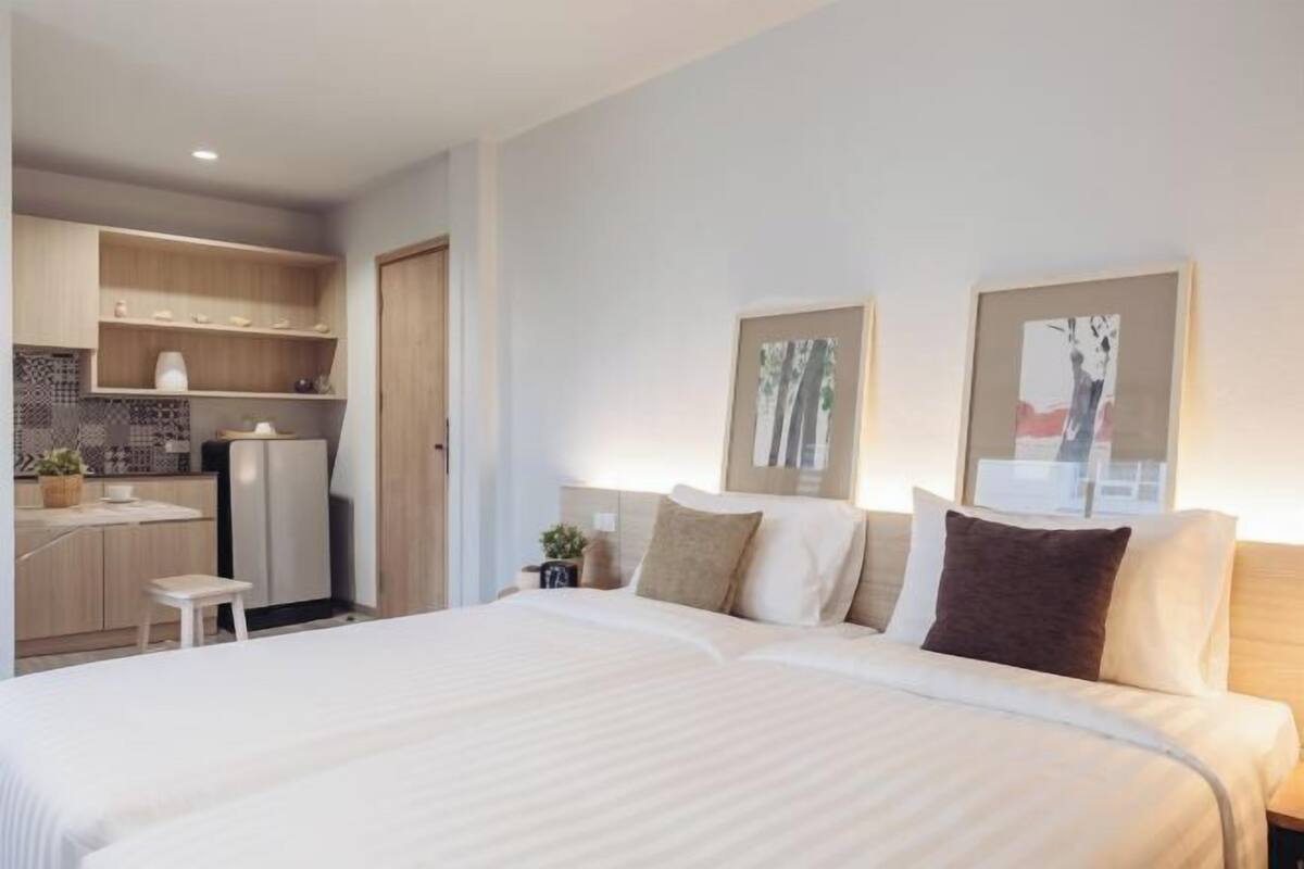 A modern hotel room with a large bed, a small kitchenette, and artwork on the walls.