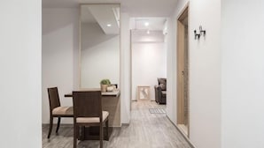 A hallway with a wooden floor, a dining area with a table and chairs, a mirror, and a door with a light switch. - China Cozy Asoke (Bangkok)