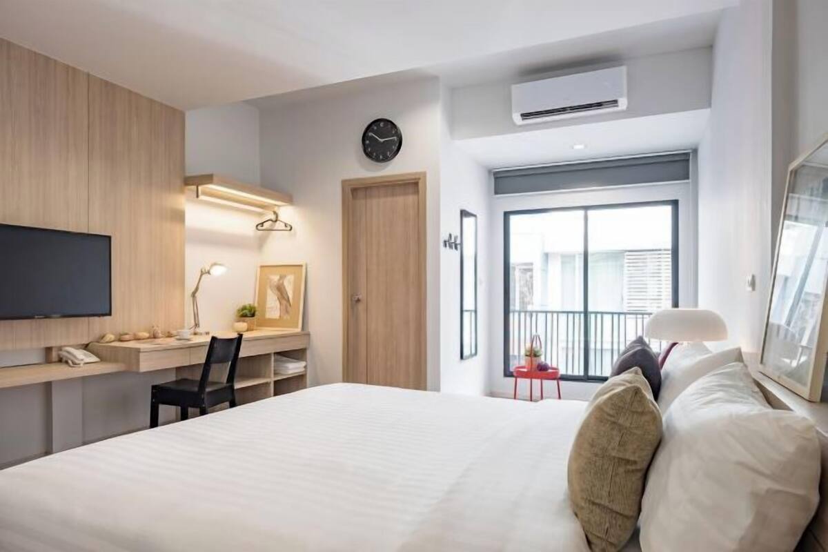 A modern hotel room with a bed, desk, TV, and a large window.