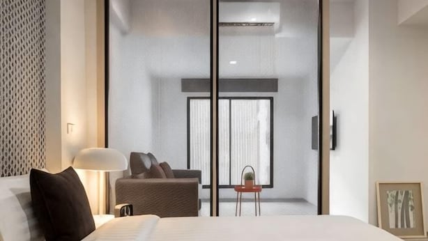 A modern hotel room with a bed, a desk, a chair, a lamp, and a view through a sliding door. - China Cozy Asoke (Bangkok)