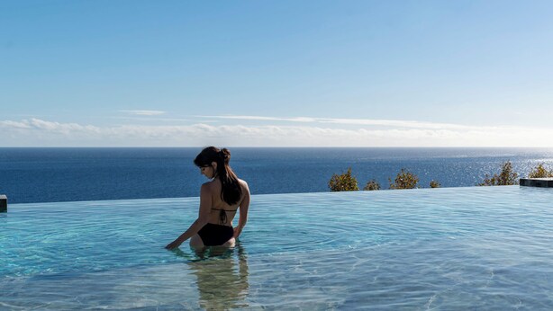 Una persona en una piscina infinita transparente con vista al océano.