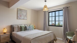 Une chambre à coucher avec un lit, des lampes de chevet, une fenêtre avec des rideaux, une chaise et un tableau au mur.