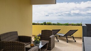 Une terrasse meublée de mobilier en osier, une table ornée d’un vase de fleurs et une vue sur la mer.