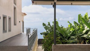 Un espace extérieur abrité avec vue sur la mer, une allée dallée et de grands plants de bananiers.