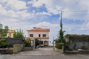 Une maison à deux étages, avec un toit en tuiles, une entrée fermée par un portail et une vue sur la mer.