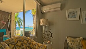 A living room with a view of the sea, a hammock, a ship's wheel lamp, and a sofa with patterned cushions. - Oceanfront Paradise: Private Balcony, Stunning Views & Steps to the Beach! (Aguadilla)
