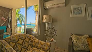 A living room with a view of the sea, a hammock, a ship's wheel lamp, and a sofa with patterned cushions.