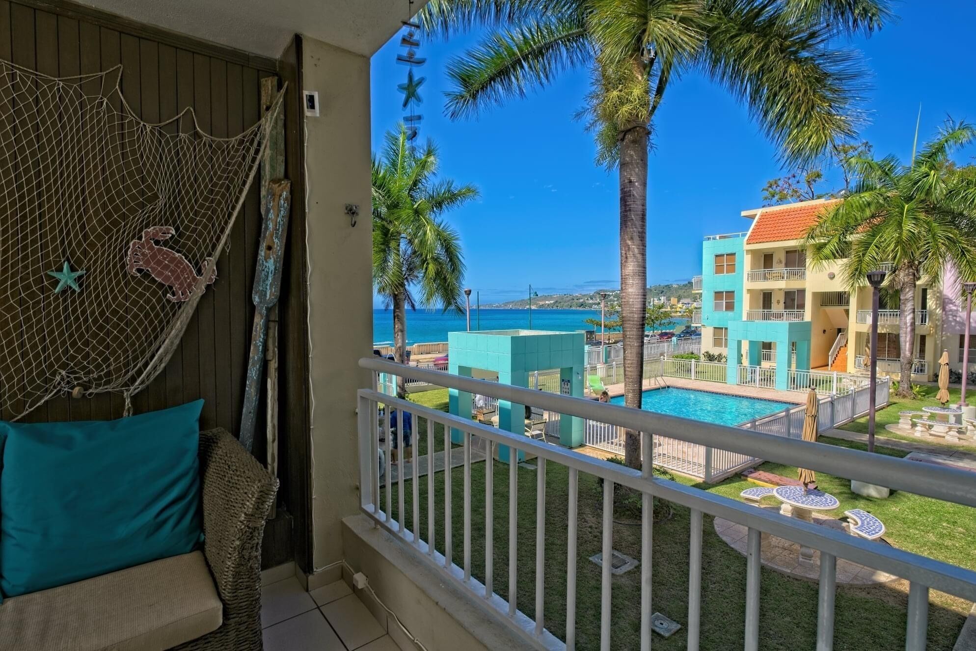 A balcony with a view of a pool, palm trees, and a building with a red roof.
