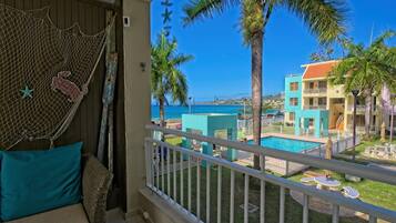 A balcony with a view of a pool, palm trees, and a building with a red roof.