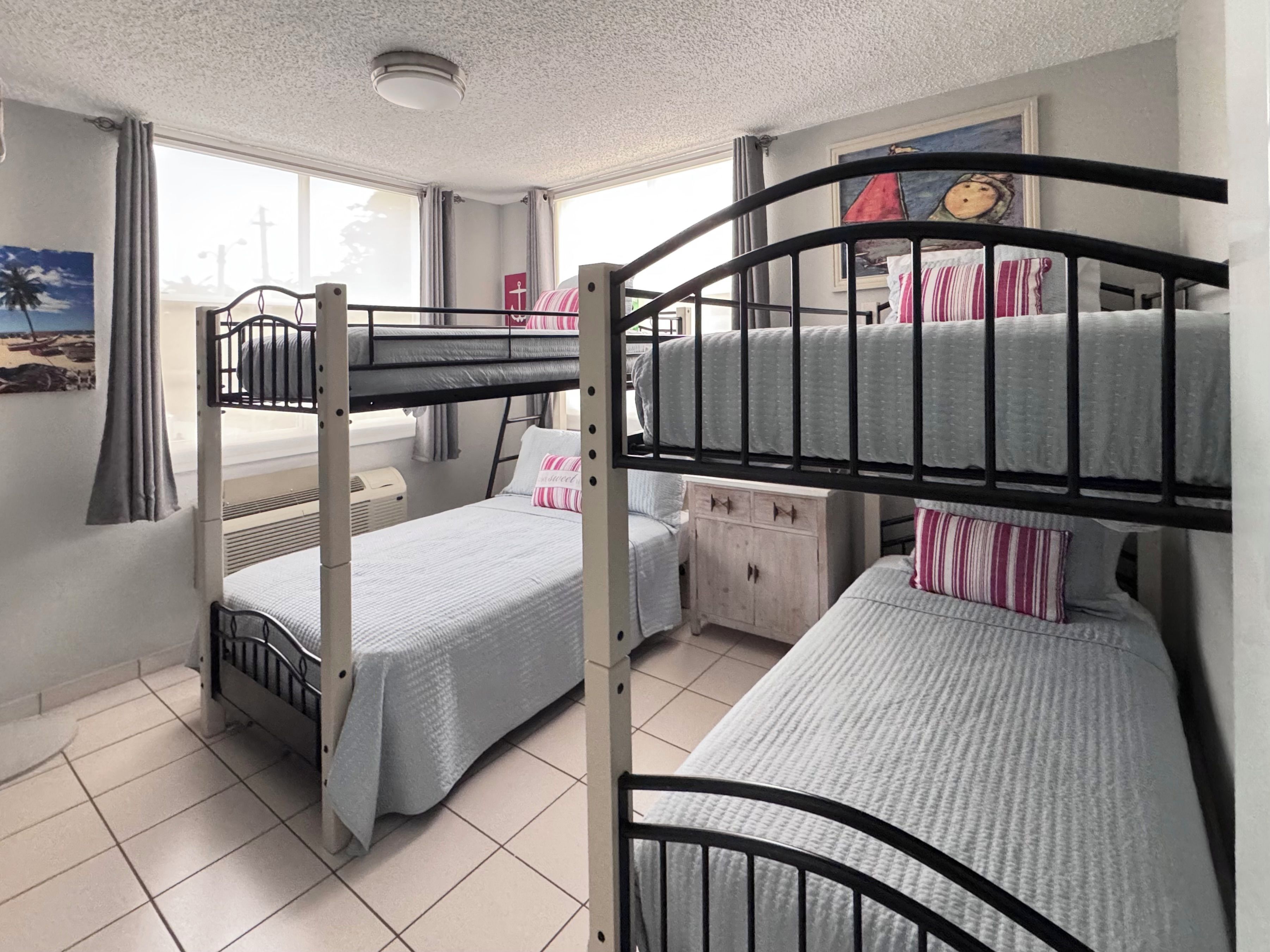 Habitación con literas, una ventana, un armario pequeño y un cuadro en la pared.