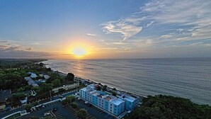 A coastal hotel with a view of the sunset over the ocean. - Oceanfront Paradise: Private Balcony, Stunning Views & Steps to the Beach! (Aguadilla)