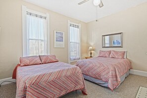 A bedroom with two beds, each with patterned bedding, a ceiling fan, and a framed picture on the wall.