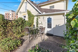 Una casa residencial con puerta de garaje, un pequeño patio con mesa y sillas, y un jardín con hiedra y flores.
