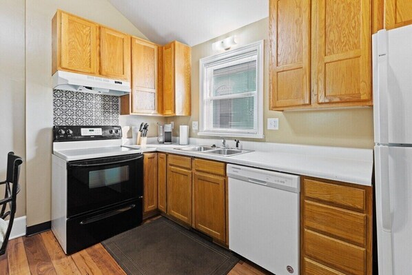 A kitchen with wooden cabinets, a black stove, a white dishwasher, and a window with blinds.