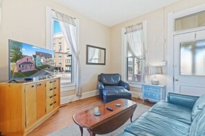 A living room with a wooden cabinet, a blue sofa, a leather chair, and a television displaying a house model.