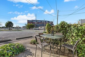 An outdoor seating area with a table and chairs, a hedge, and a building in the background.