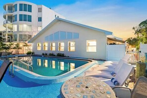 A modern building with a swimming pool, lounge chairs, and a sun terrace.