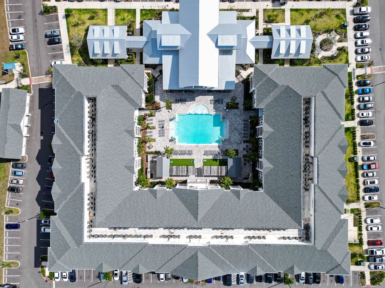 An aerial view of a hotel with a central swimming pool, multiple parking lots, and a distinctive modern architectural design.