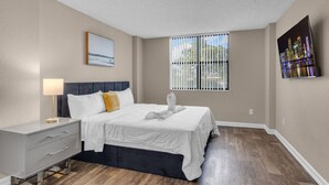 Un dormitorio con cama, mesita de noche, lámpara y ventana con persianas.