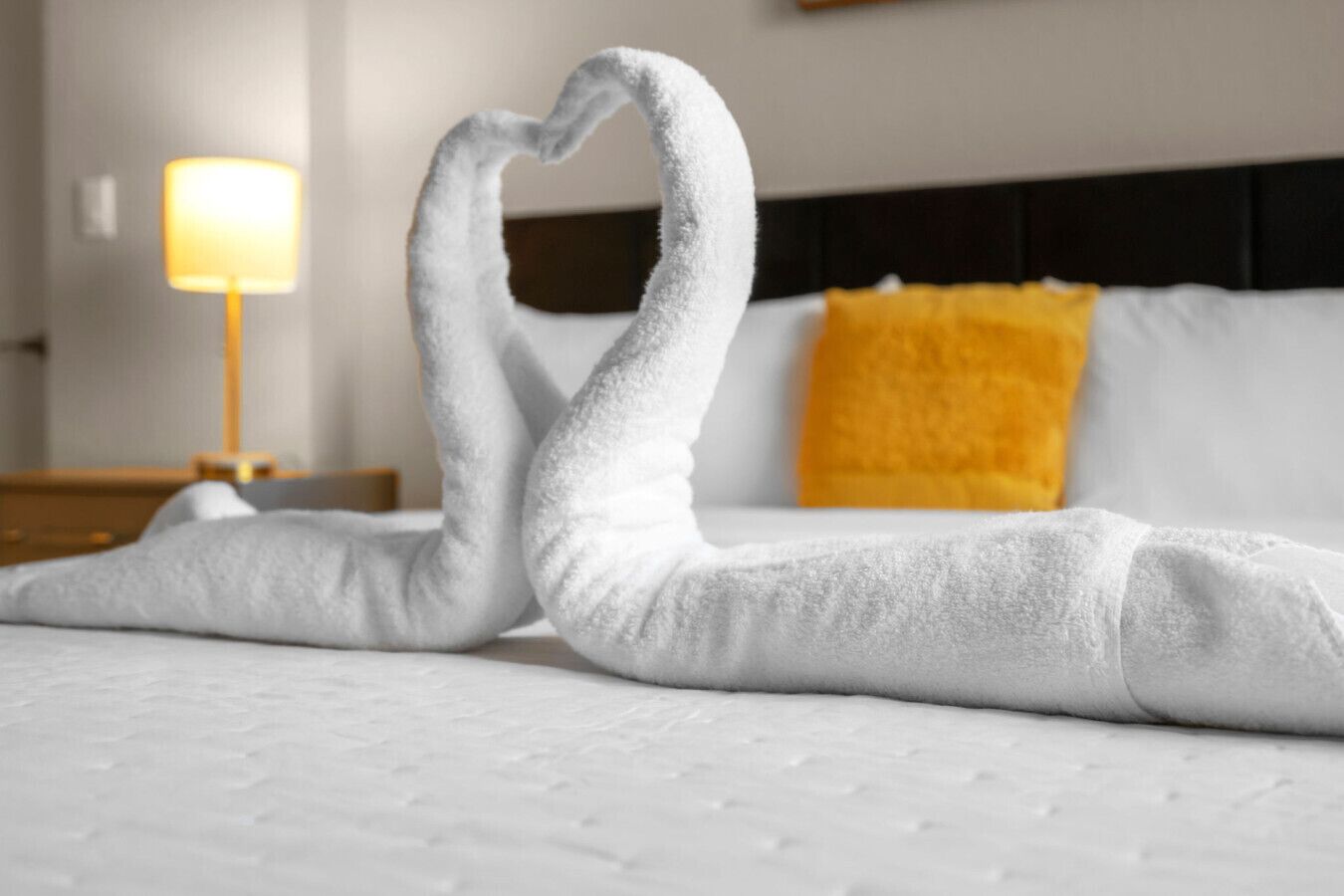 A bed with a white duvet and a single yellow pillow.