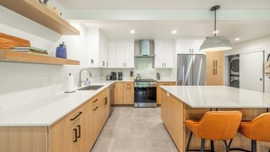 A modern kitchen with white cabinets, a central island, orange bar stools, and a hanging pendant light. - Mountain Modern 3-bedroom Lower DV/Old Town Condo (Park City)