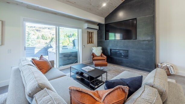 A modern living room with a fireplace, a large window, and a ceiling fan. - Mountain Modern 3-bedroom Lower DV/Old Town Condo (Park City)