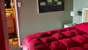 A bedroom with a red bedspread, a painting on the wall, and a nightstand with a lamp. - Loft with incredible lake views (San Carlos de Bariloche)