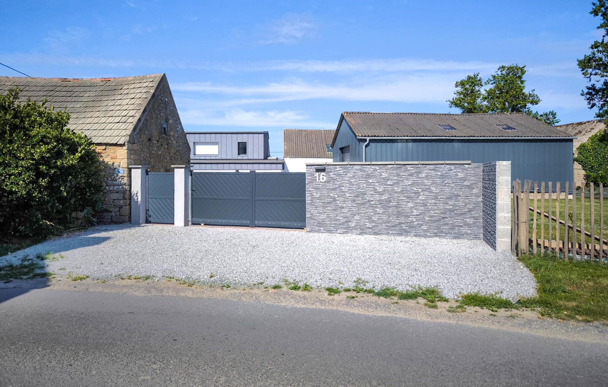 A residential property with a gravel driveway, a stone wall, and a metal gate.