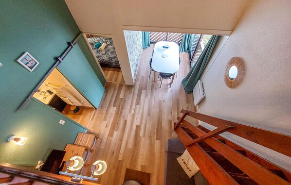 Una habitación con piso de madera, una mesa blanca con sillas y vistas al exterior a través de una ventana.