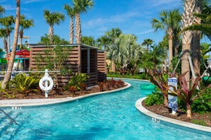 Une piscine dotée d’une structure en bois, de palmiers et d’un poste de surveillance pour les sauveteurs.