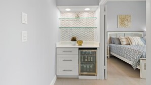 Une chambre compacte comprenant un lit, des tables de chevet, un mini-réfrigérateur encastré et une étagère murale agrémentée d’objets décoratifs.