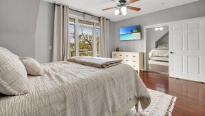 Un dormitorio con cama, ventilador de techo, televisor y vistas al exterior.