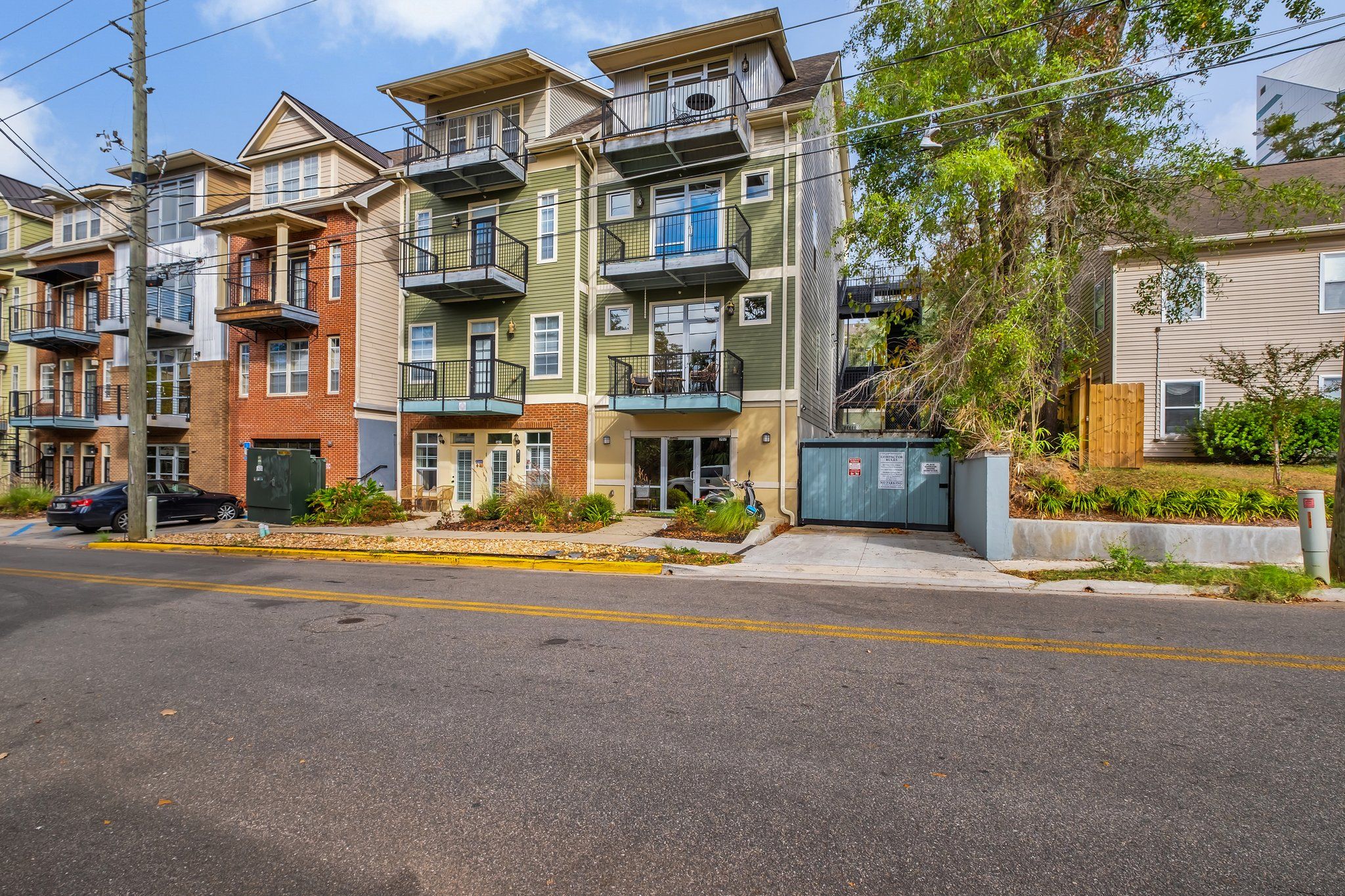 A row of multi-story residential buildings with balconies, a gated entrance, and a street in front.
