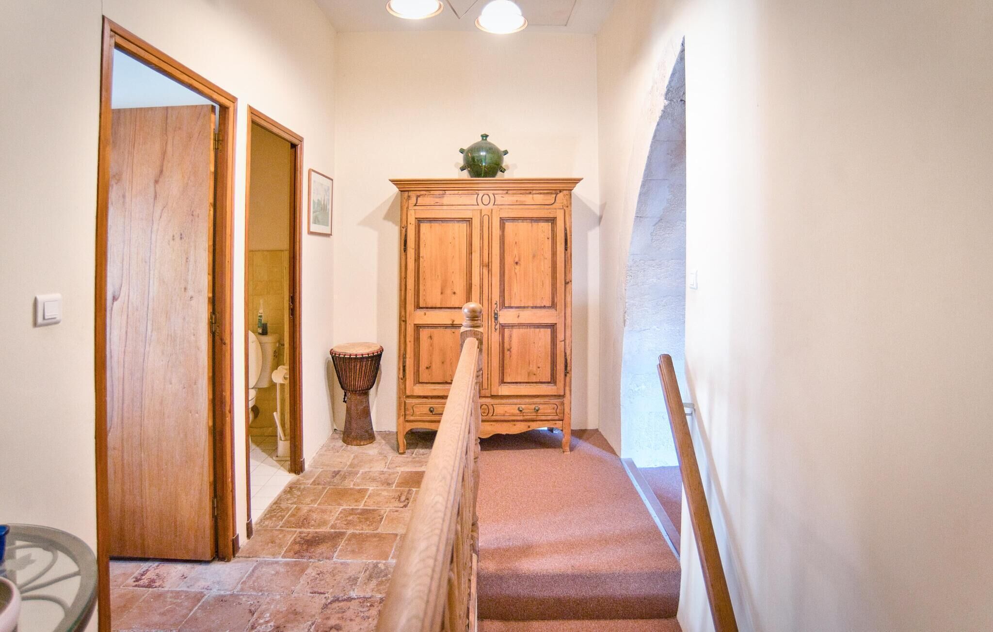 A narrow hallway with a wooden door, a small drum, and a cabinet with a green object on top.