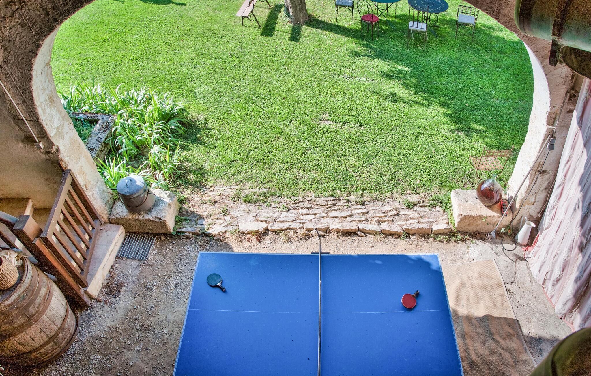 A courtyard with a blue ping pong table, a stone wall, and a grassy lawn.