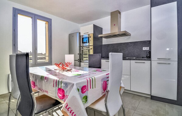 Een moderne keuken met roestvrijstalen apparatuur, een eetgedeelte met een tafel met een kleurrijke tafelkleed, en uitzicht door het raam.