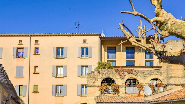 A multi-story building with a flat facade, multiple windows with shutters, and a satellite dish on the roof. - Beautiful apartment in Uzès with WiFi (Uzès)